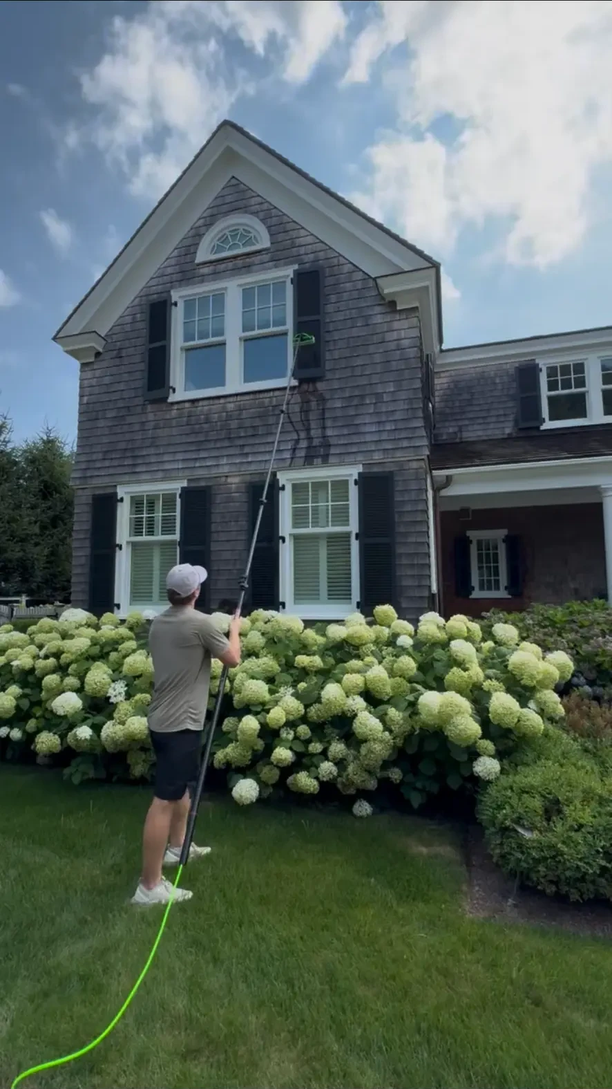 Hayden cleaning windows of a shingled South Shore home with a water-fed pole